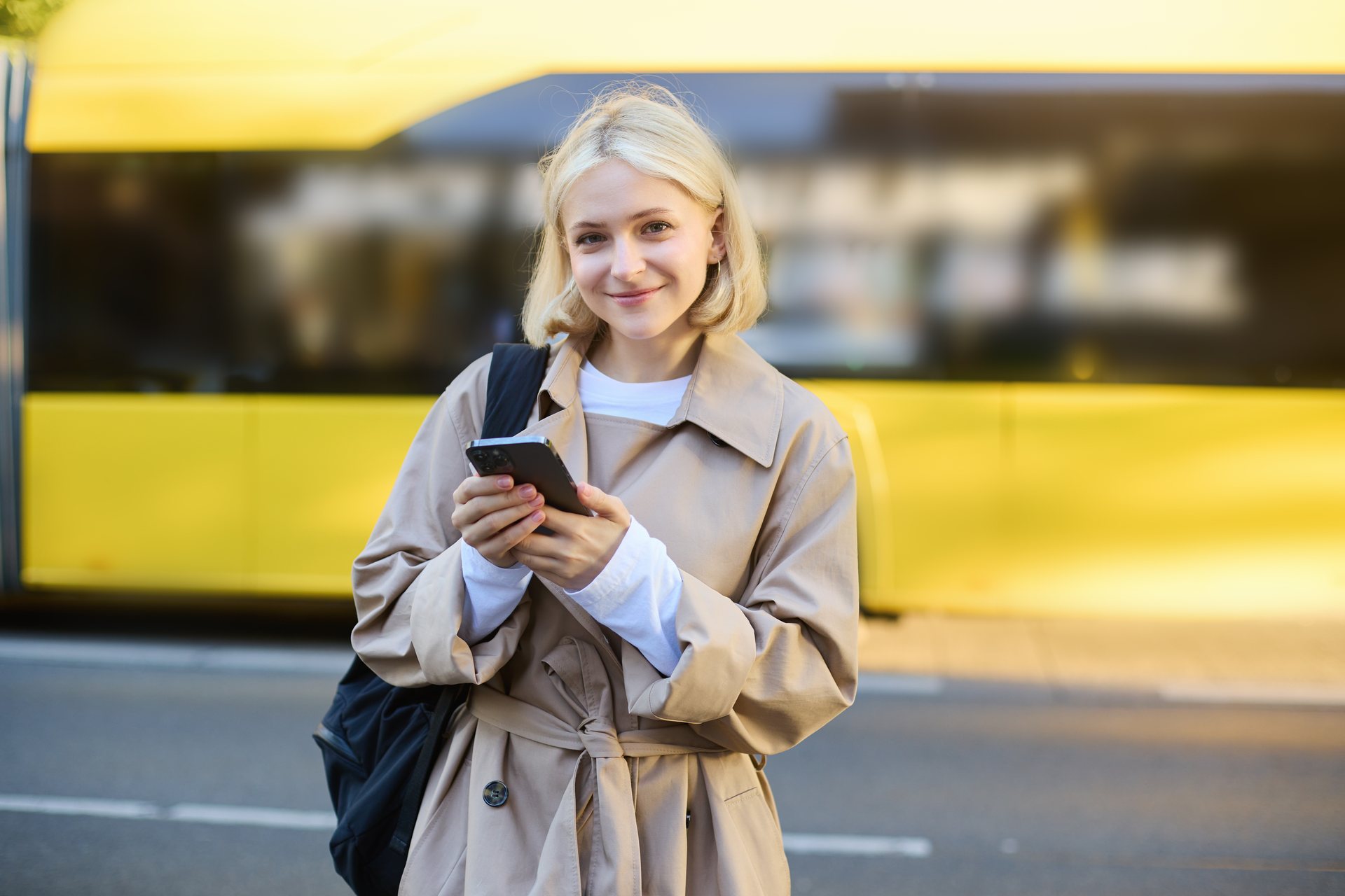 Studentka z telefonem czeka na przystanku przed autobusem