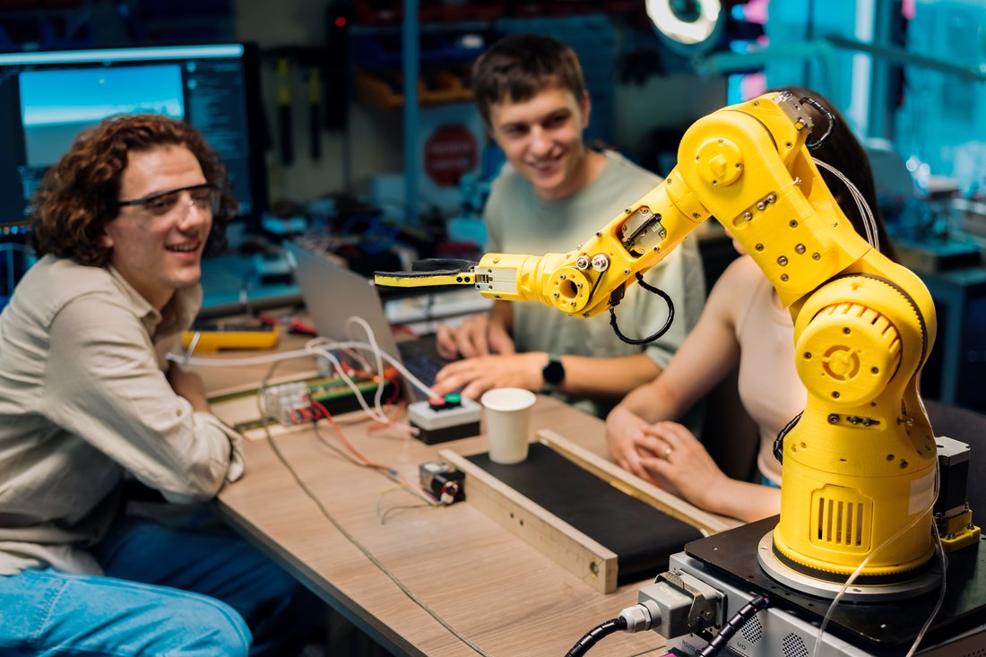 Studenci w okularach ochronnych pracują przy ramieniu robota